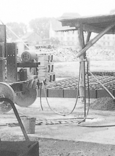 Eine historische Schwarz-Weiß-Fotografie mit Fokus auf frühen industriellen Fertigungsmaschinen mit großen Rädern und einem Elektromotor auf einem Schiedel-Außenproduktionsgelände.