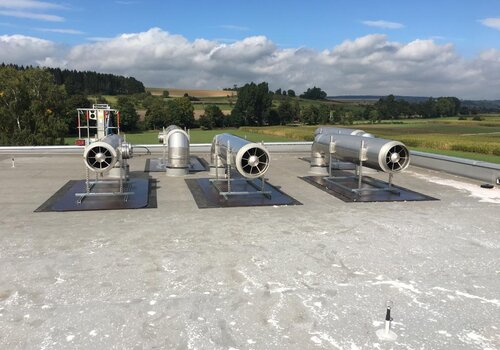 Mehrere Abgasschalldämpfer auf einem Dach eines Industriegebäudes